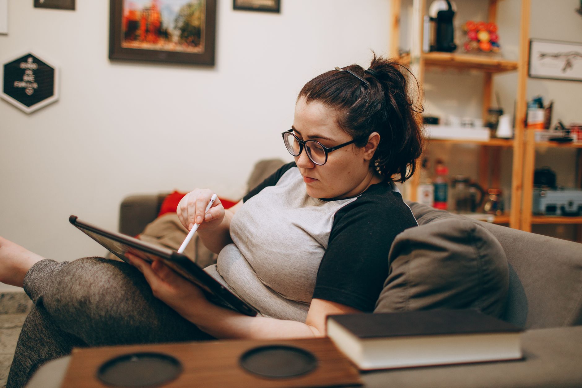 Frau mit Brille entspannt auf dem Sofa und informiert sich am Tablet über ein digitales Zusatzeinkommen.