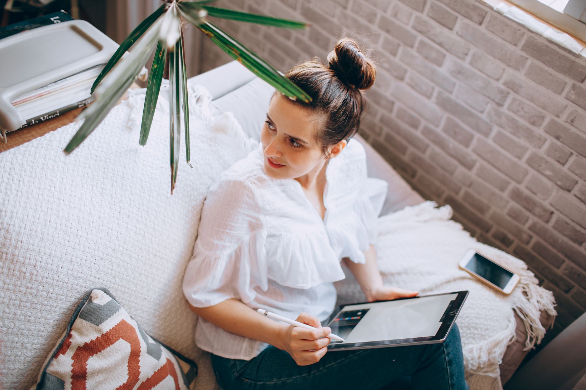 Frau surft von der Couch aus mit Tablet und Smartphone im Internet.