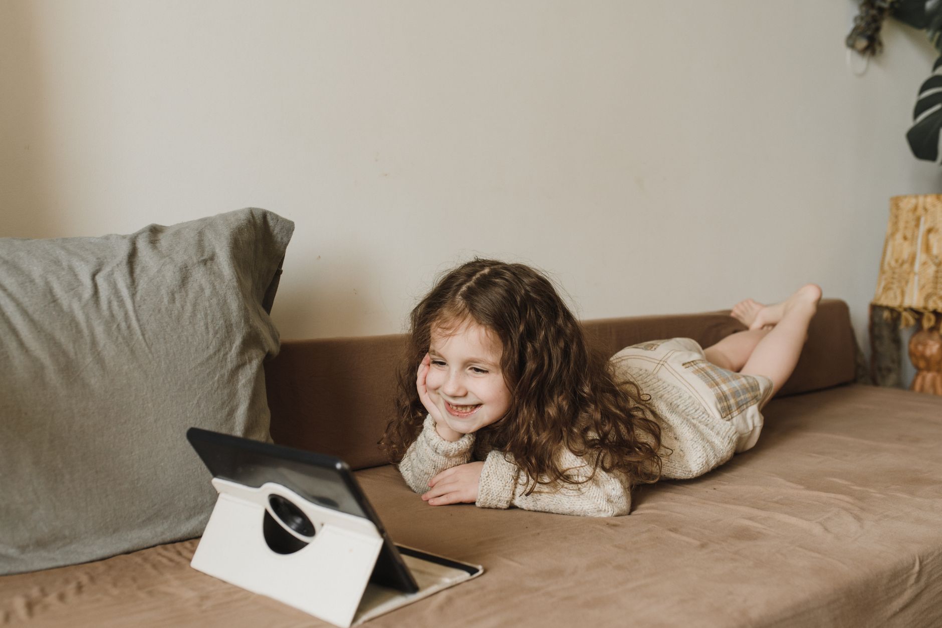 Kind schaut zufrieden ein Tablet an, während es zuhause auf dem Sofa liegt.