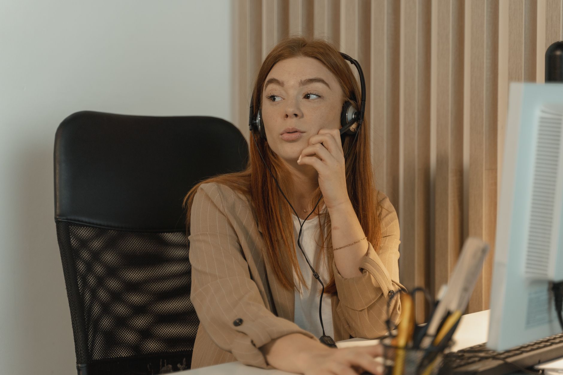 A review specialist in a headset sits at a desk beside a monitor, glancing aside between calls.