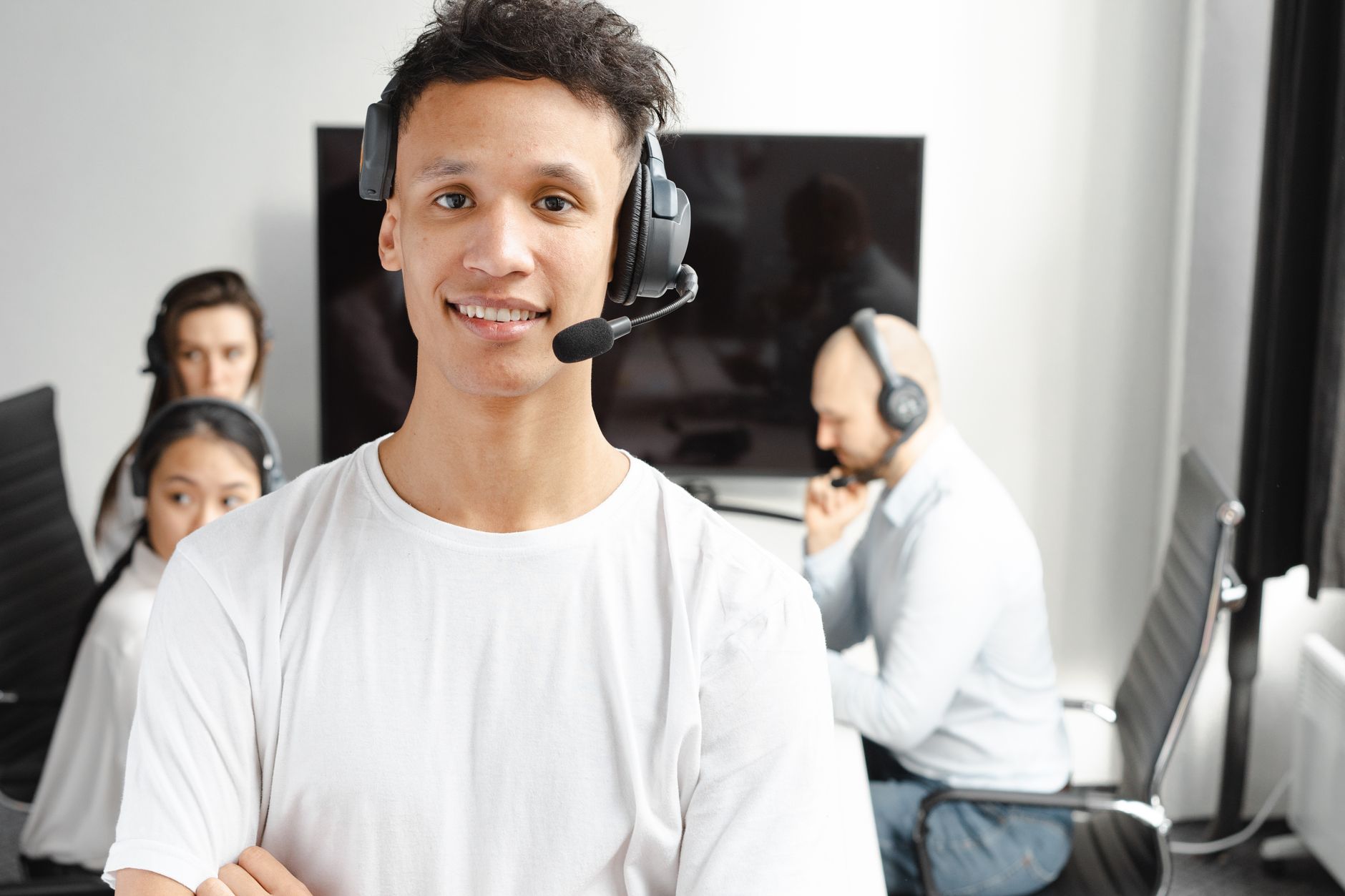 A smiling member of a consultation desk team in a headset, with colleagues on calls in a bright office behind.